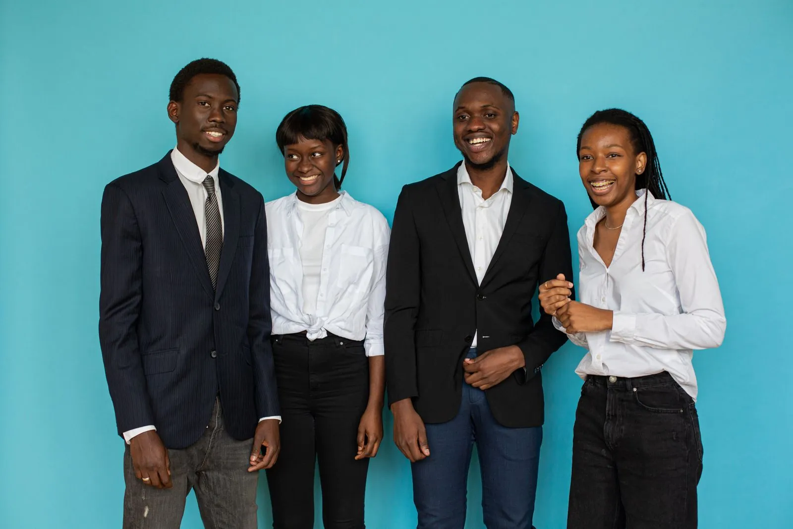 Quatre jeunes professionnels souriants, en costume et en chemisier, devant un fond bleu-vert