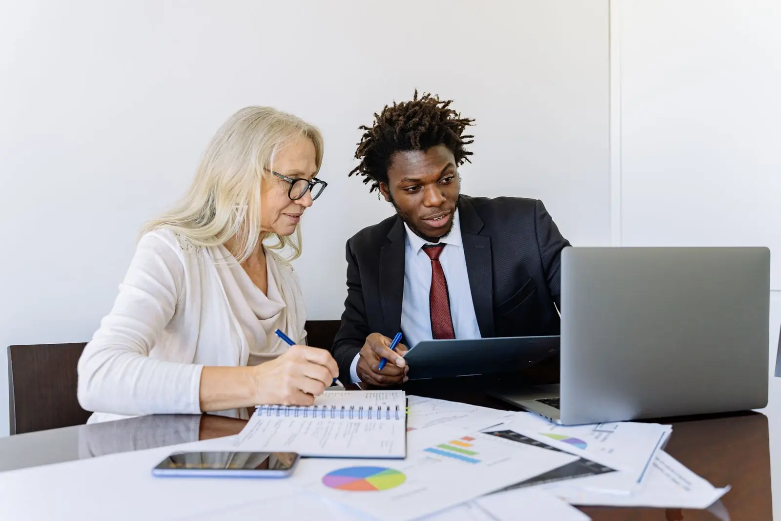 Un conseiller et une cliente étudient ensemble des graphiques et des documents financiers devant un ordinateur portable
