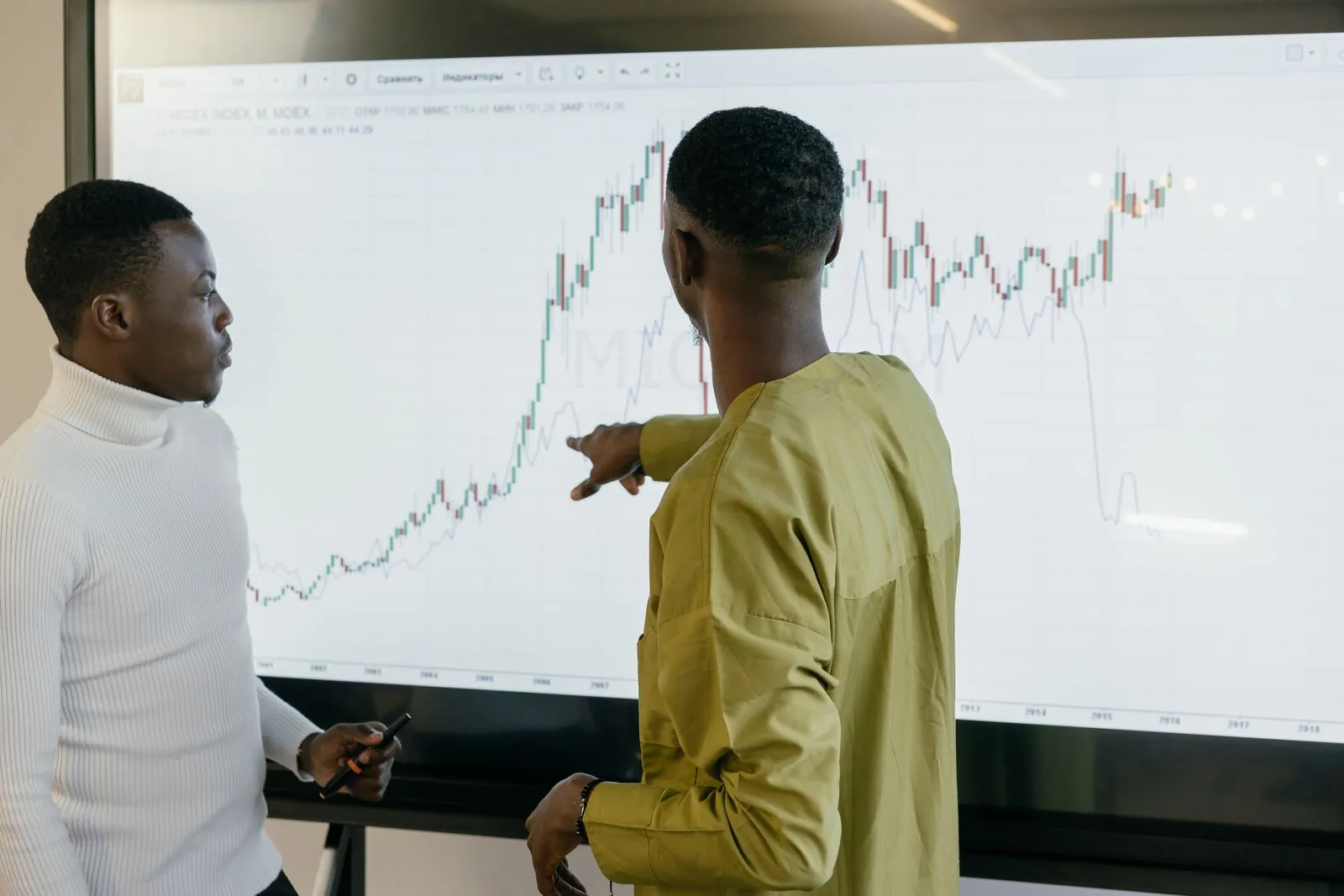 Deux professionnels commentent une courbe financière sur un grand écran
